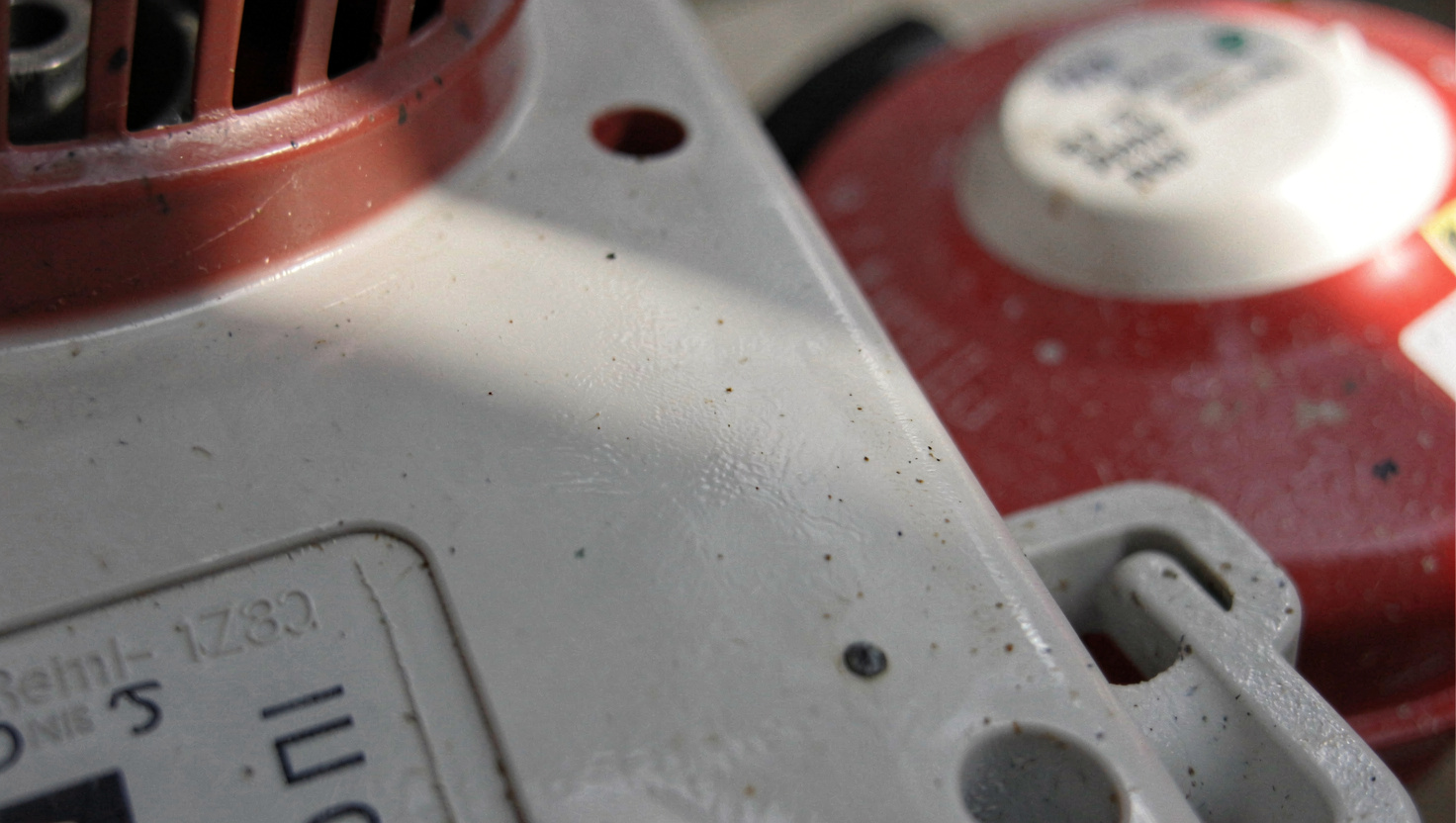 A hydrogen dispenser nozzle locked into a car's receptacle at a fuelling station at dusk, the hose curving down from the pump, shot from the driver's side at waist height.