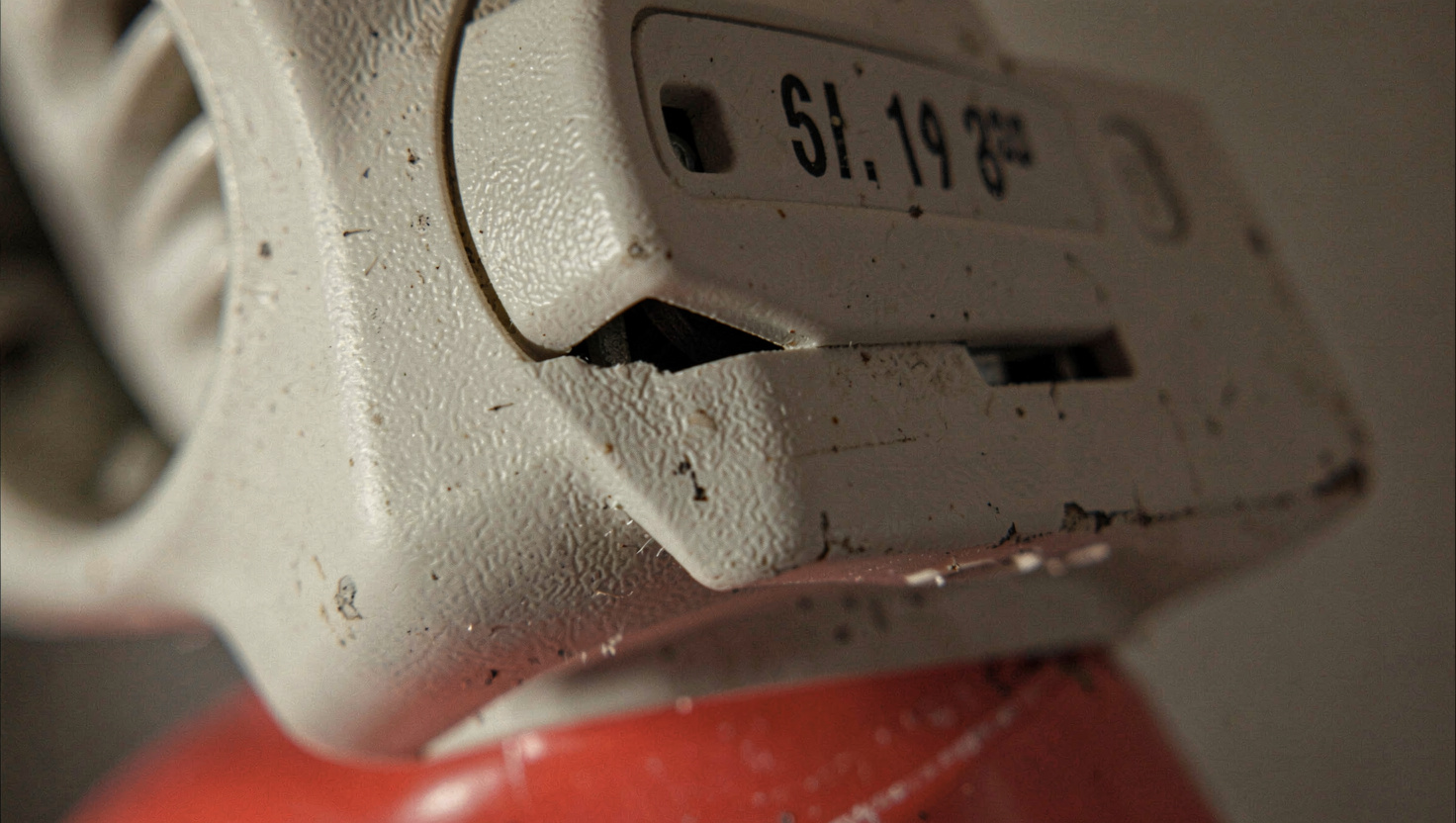 A cutaway view of a wood frame exterior wall in a garage workshop, showing fiberglass batts between studs, a foil facing, and sheathing, lit by a work lamp from the left at close range.